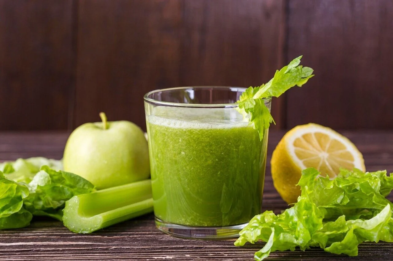 Fresh green smoothie made with celery, apple, lettuce, and lemon, garnished with a celery stick